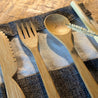 A Sarita bamboo flatware set lies open on a mango wood table
